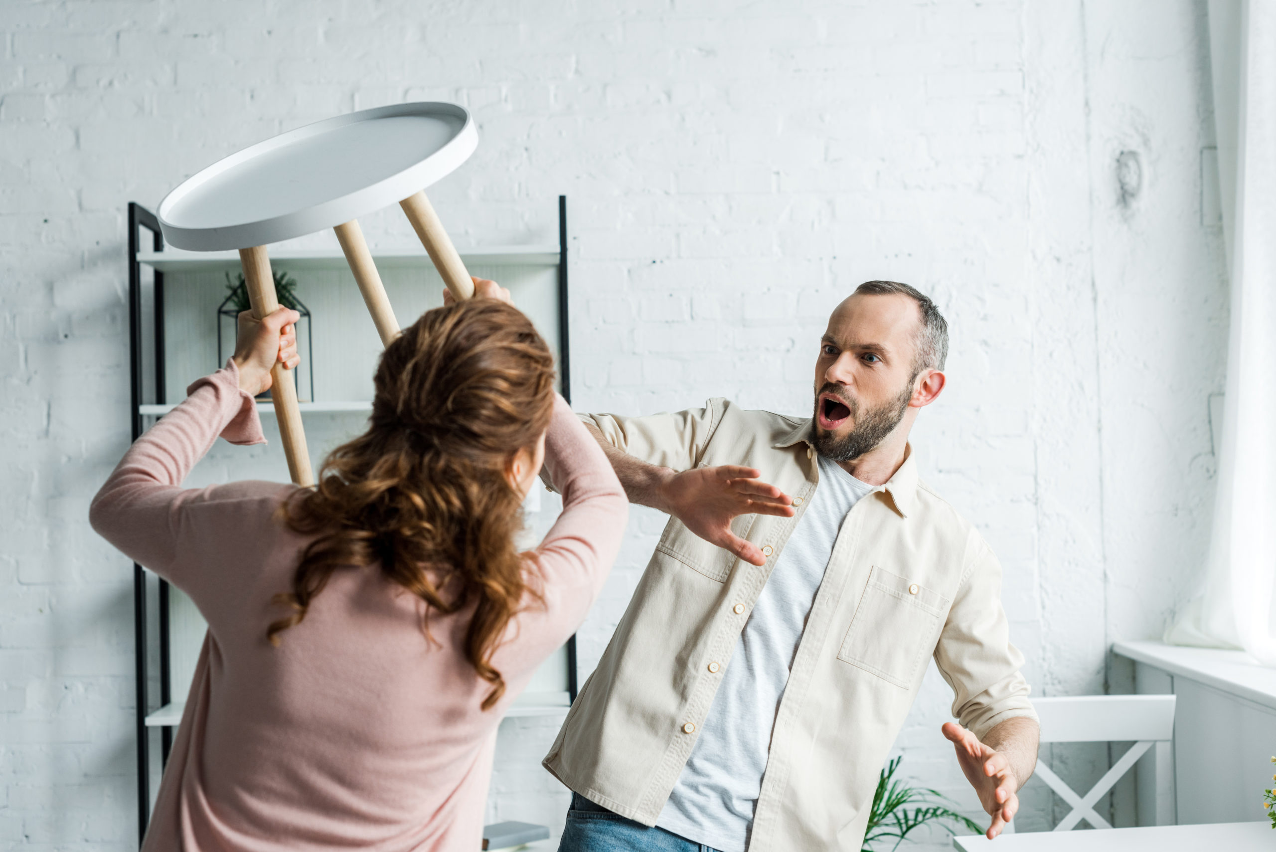defensive man looking at angry woman throwing a stool